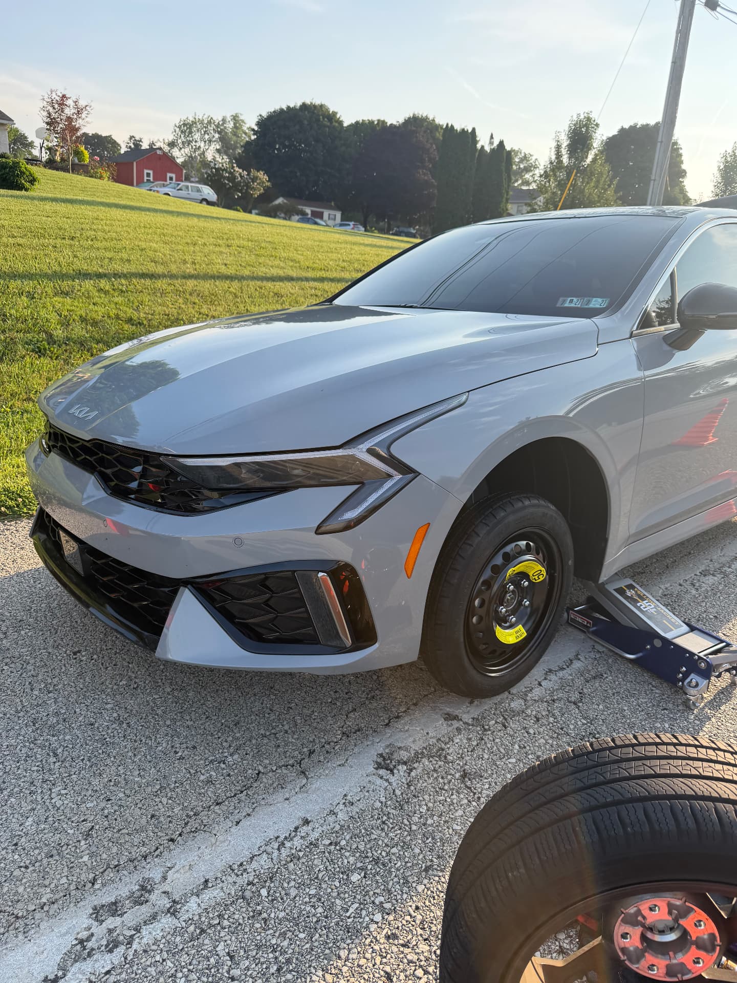 Kia K5 raised on a floor jack with the spare wheel installed during a mobile tire change