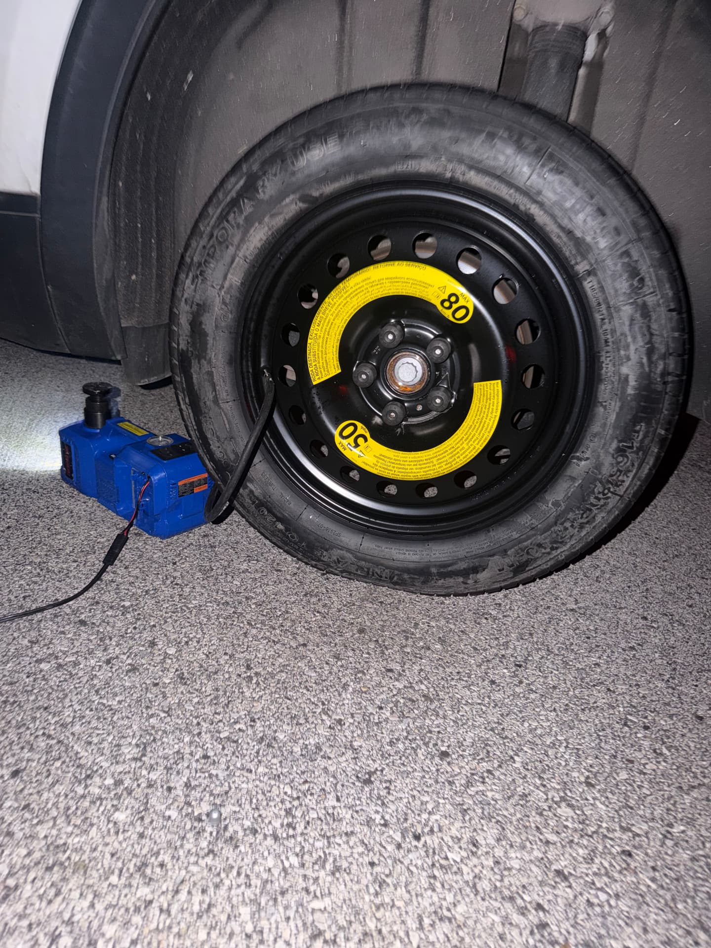Spare tire mounted at night with a portable jack and inflator during a roadside tire change