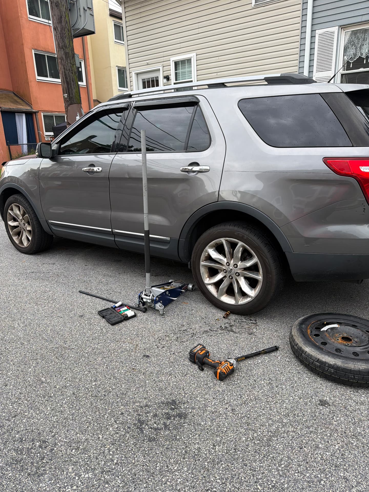 MR RESCUE technician changing a flat tire on a Ford Explorer with a floor jack and impact wrench