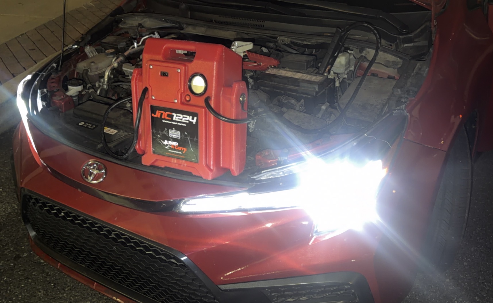 Jump pack connected to a Toyota Corolla battery for a mobile jump start at night